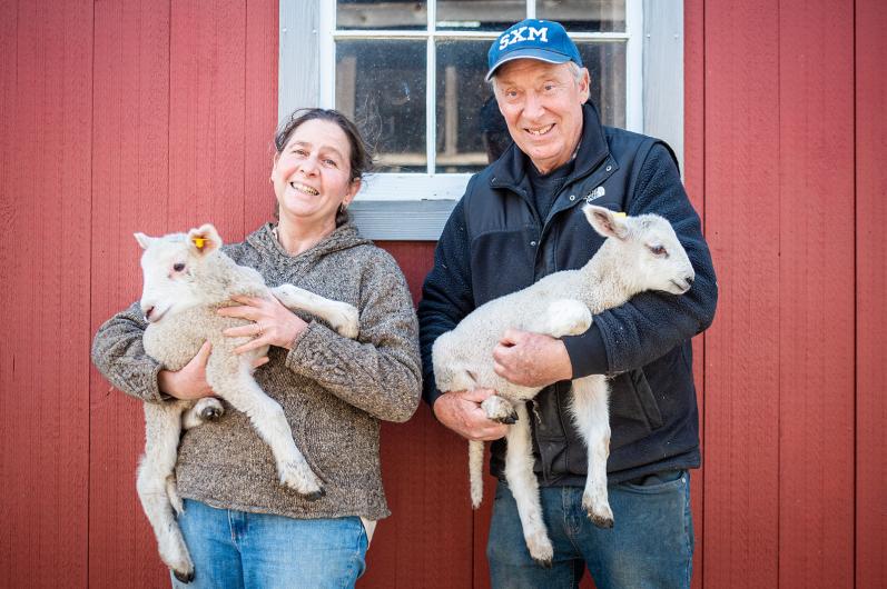 Christa and Arnie Fischer of Flat Point Farm holding lambs by their barn.