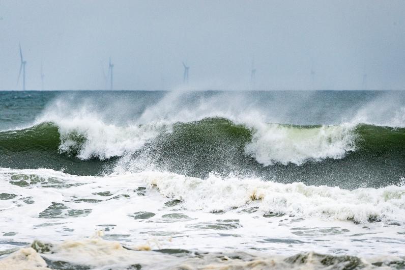 Waves break with wind turbines in the background.