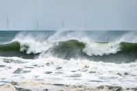 Waves break with wind turbines in the background.