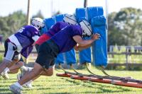 Football players line up and hit the sleds.